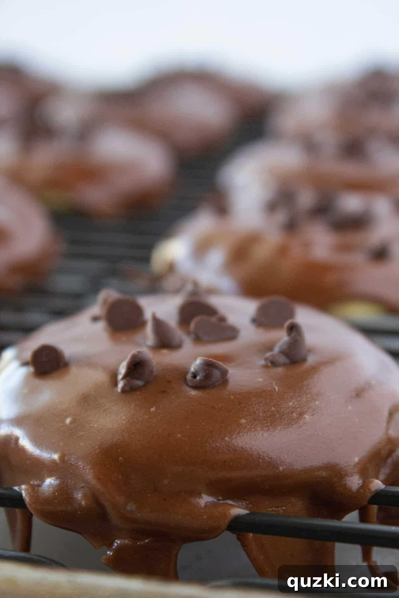 Rich cooked chocolate frosting being spooned over Chocolate Chip Sheet Cake Cookies on a cooling rack.